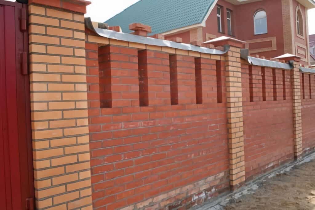 Dacha typique d'une personne riche dans les années 90 : une maison de brique rouge qui est cachée derrière une haute clôture en briques rouges