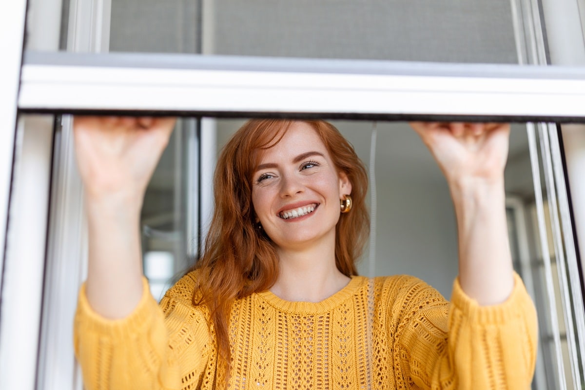 femme qui ferme une moustiquaire de fenêtre