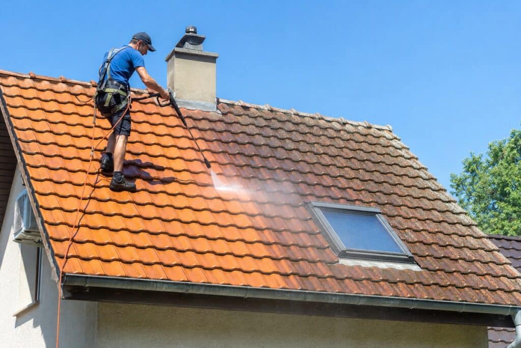 homme qui nettoie une toiture avec un nettoyeur haute pression