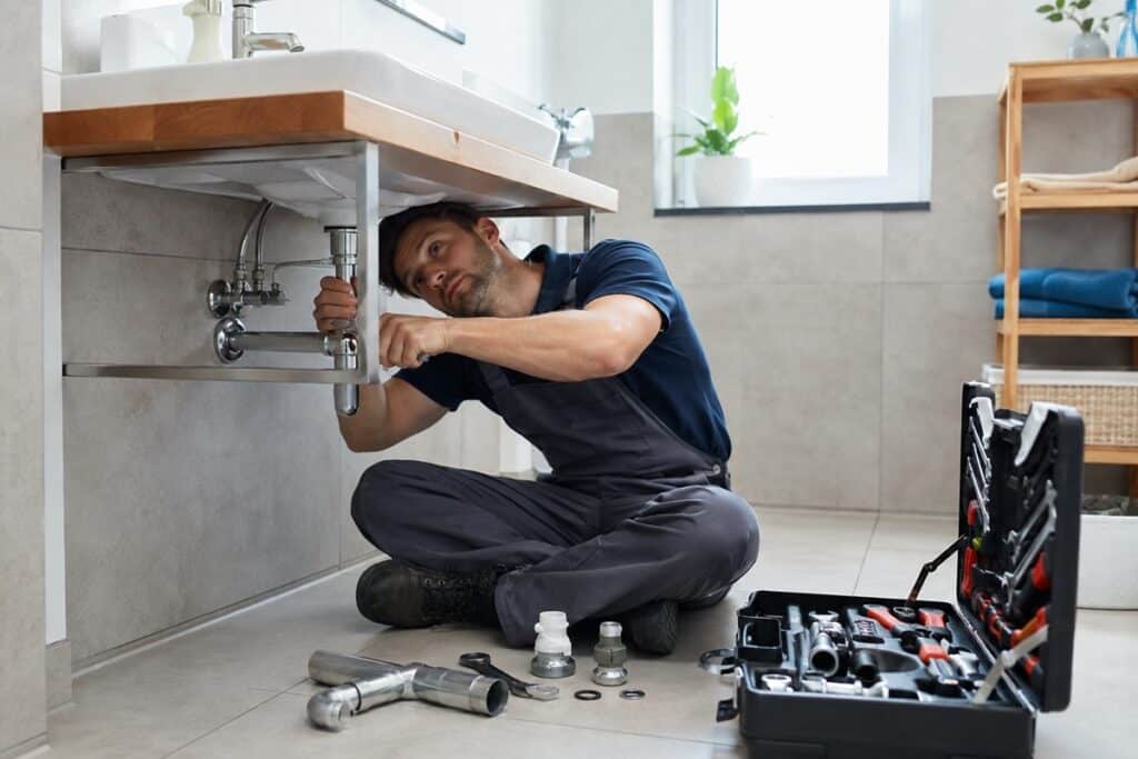 plombier qui répare une canalisation sous un évier