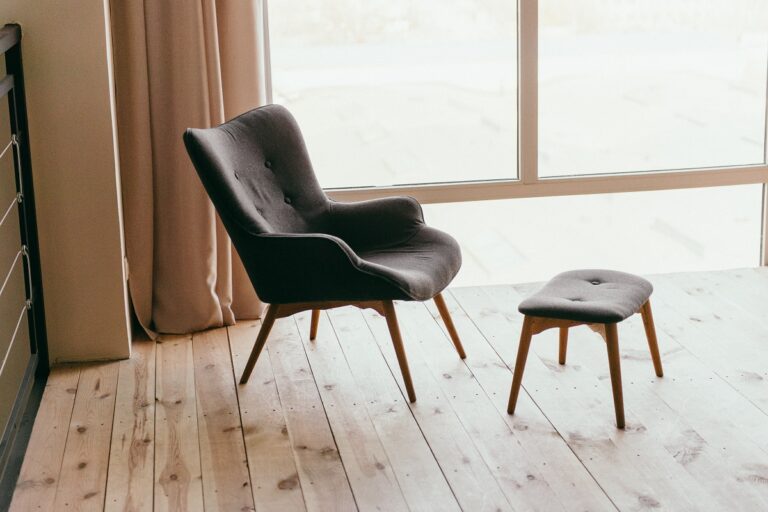chaise scandinave et repose pied devant une baie vitrée